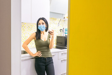 Fototapeta na wymiar Attractive dark-haired caucasian woman stands in the kitchen and holds confidently a glass of red wine making a toast. Self isolation and postivity duirng pandemic.