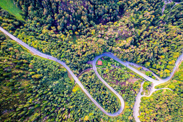 Winding Road surrounded by a colourfull trees in the forest. Aerial drone view. Kesselberg