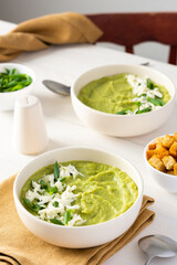 Healthy delicious broccoli and cucumber cream puree soup with mozzarella, green onions and croutons, bowl of soup on a white table