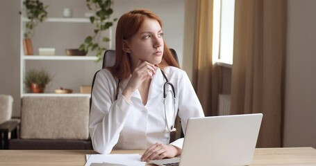 Concentrated young professional general practitioner woman in white uniform looking at laptop screen. Thoughtful medical female worker planning working schedule in computer, think about diagnosis - Powered by Adobe