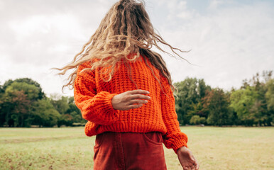 Horizontal image of an young woman with blowing long blonde hair wearing an orange sweater posing...