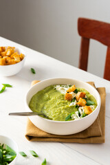 Healthy delicious broccoli and cucumber cream puree soup with mozzarella, green onions and croutons, bowl of soup on a white table