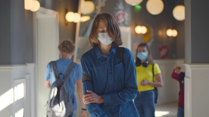 Upset schoolboy in safety mask walking in school corridor.