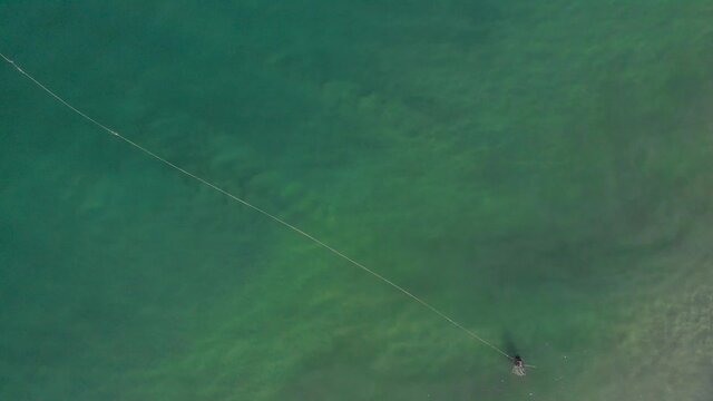 Aerial top down view of fisherman collecting the string of the net laid over the surface of water in ocean.