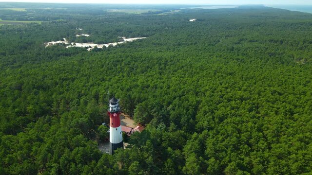 Drone slow pull out from Stilo Lighthouse and green forest around it - lighthouse located in Osetnik (formerly Stilo) on the Polish coast of the Baltic Sea, close to the village of Sasino, aerial