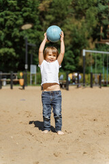 little girl in a white t-shirt with a blue ball on the beach. Active childhood and sports passion concept