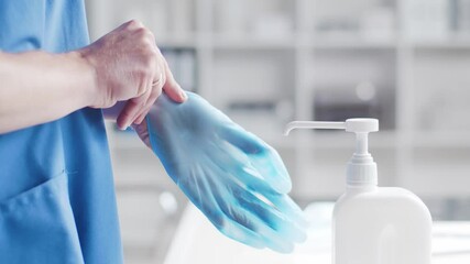 Close-up of doctor putting on gloves and cleaning hands using disinfectant with medical soap. Office in hospital on the background.
