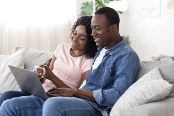 Happy black couple websurfing, using laptop at home