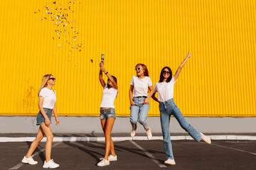Happy young women friends having fun with confetti on background of yellow wall of shopping mall,...