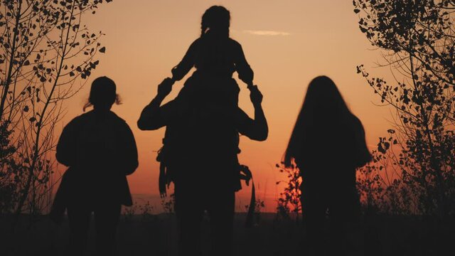 happy family tourists go hiking in park sunset silhouette. adventure travel concept. teamwork. happy family sun a tourists with backpacks hikers go camping. group people teamwork walking park