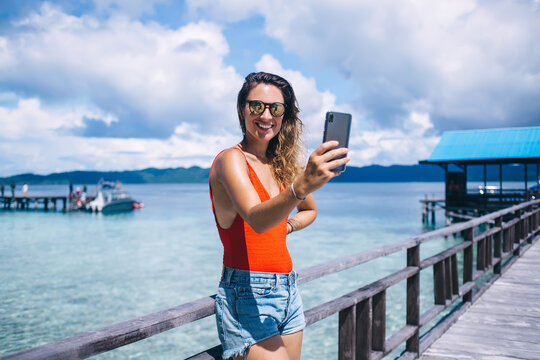 Half length portrait of happy girl posing while creating selfie content for making vlog about trip to Maldives, cheerful woman with modern smartphone technology taking pictures via mobile app