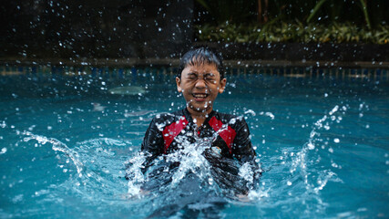 Happy boy kid playing water splashing in swimming pool. Asian kid