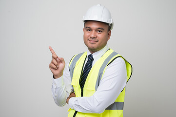 Asian worker in uniform hard hat pointing the finger to blank space for advertise text or mockup in studio isolated white background.