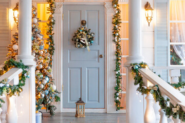 Fototapeta na wymiar Christmas porch decoration idea. House entrance decorated for holidays. Golden and green wreath garland of fir tree branches and lights on railing. Christmas eve at home.