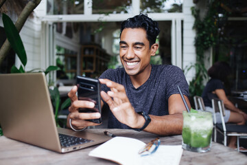 Happy ethnic man interacting with smartphone on terrace