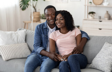 Happy african american couple cuddling on sofa at home