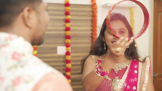 Shoulder shot, Indian woman in traditional dress seeing her husband or partner through sieve during Hindu Indian religious karwa chauth festival at home