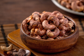 Cashew nuts with peel in a wooden bowl on wooden tray and table background, healthy raw food plate.