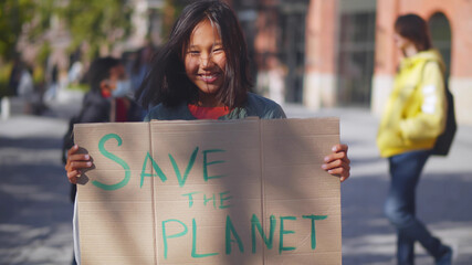 Portrait of asian schoolgirl showing sign with save the planet text protesting against pollution