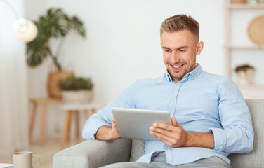 Happy guy using digital tablet sitting on the couch