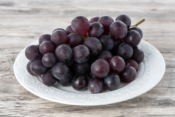 Delicious bunch of grapes fruit on a plate over wooden table background.