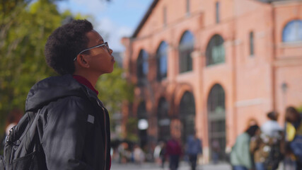 African schoolboy going to school standing outdoors and looking at brick building