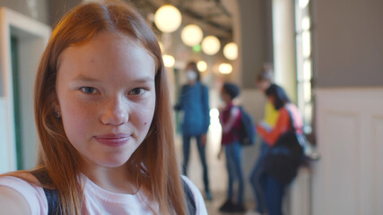Redhead teenage student girl taking selfie or talking on video call in corridor