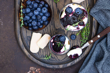 Dessert from mascarpone or ricotta cheese, blueberries and biscuit in glass on dark concrete background. No baked cheesecake or tiramisu. Top view.