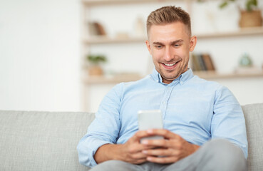 Closeup of smiling guy using smartphone at his home