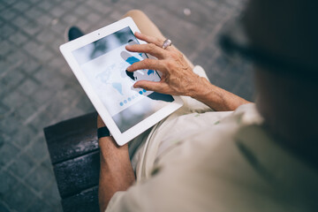 Crop anonymous man touching screen of tablet on bench