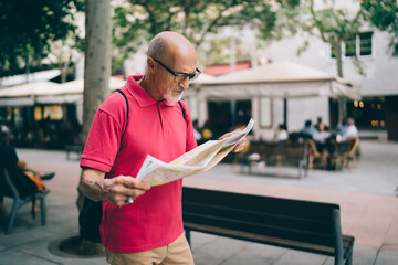 Serious senior man in eyeglasses searching location on map