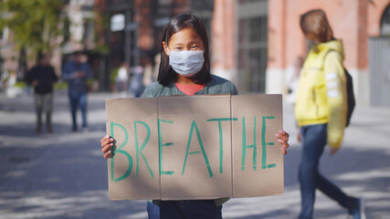 Portrait of asian school child in safety mask holding cardboard with inscription breathe