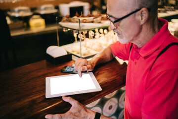 Male senior using mock up touch pad with blank screen and copy space area for your internet advertising, man connecting to 4g wireless on modern digital tablet for installing application notification