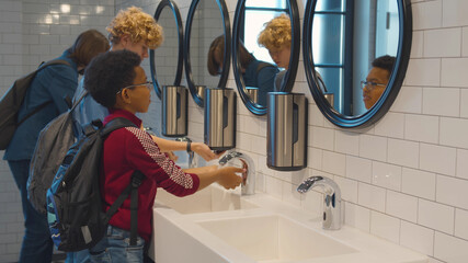 Diverse schoolboys washing hands after using toilet in school washroom