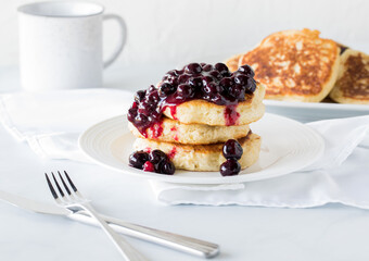 A fresh stack of fluffy pancakes topped with warm blueberry sauce and more pancakes in behind.