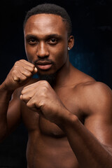 dark-skinned handsome man with a naked sports torso.against a dark background, he looks at the camera with folded arms like a boxer