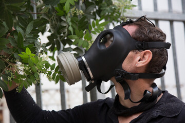 Handsome man in a protective gas mask, virus protection concept. Holding a flower in his hand and sniffing through a gas mask