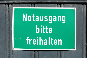 Grünes Schild Notausgang bitte freihalten an einer dunklen Holztür,  Deutschland