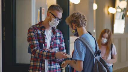 Young male teacher in mask scanning temperature of student with contactless thermometer