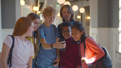 Multiethnic friends in school corridor enjoying watching text or video on mobile phone