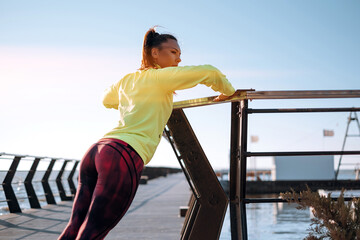 outdoor workout concept. young woman in tracksuit performs sports workout on the pier
