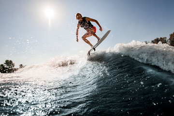 view of man jumping over river wave on board against sunny blue sky.