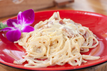 Closeup Spaghetti Carbonara in red plate on wooden table at the restaurant.