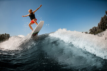 great view of man jumping over river wave on board against sunny blue sky.