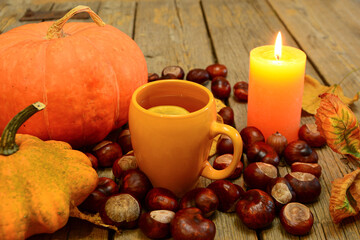 Autumn composition. Orange cup, mug of tea with lemon with pumpkins, chestnuts, yellow leaves and candle on wooden background. Autumn  card, composition, mood.  