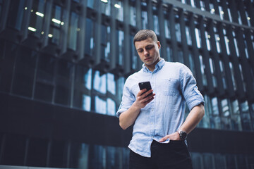 Serious young guy using smartphone in business district