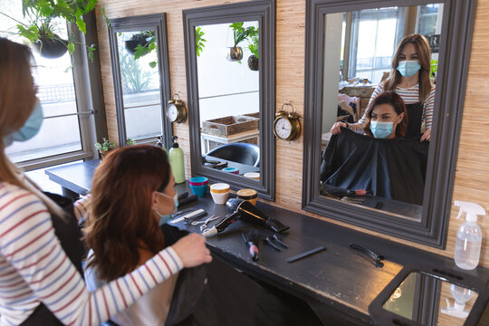 Female hairdresser wearing face mask putting cape on female customer at hair salon