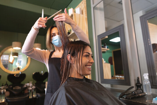  Female hairdresser wearing face mask cutting hair of female customer at hair salon