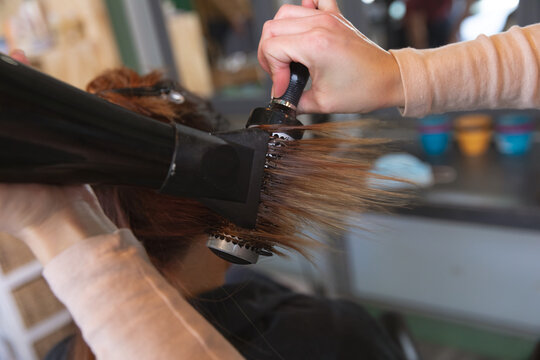 Mid section of female hairdresser blow drying hair of female customer at hair salon