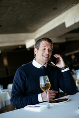 Handsome businessman dressed in the suit drinking wine. Businessman talking to the phone..